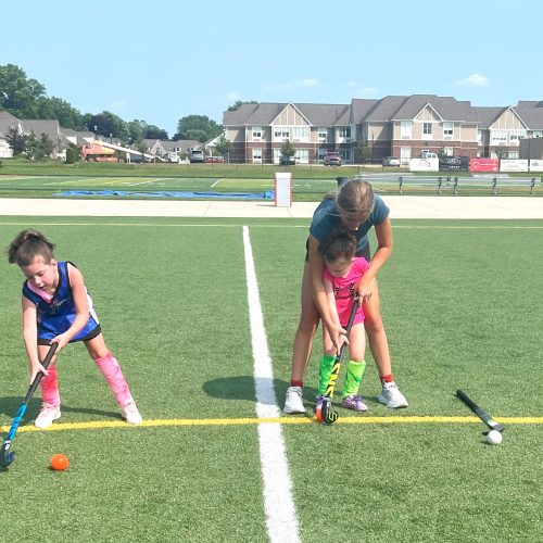 photo of a great lakes regional field hockey high school players helping a youth player at summer field hockey camp