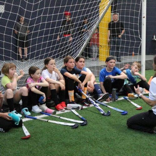 group of youth field hockey players listening to a coach